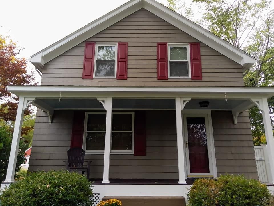 Tan clapboard home with a white porch and red shutters, repainted by Mario Mattiace of Genesis Painting